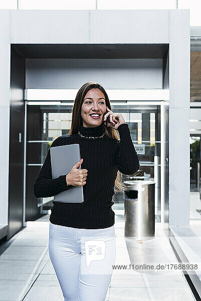 Happy businesswoman with laptop talking on mobile phone