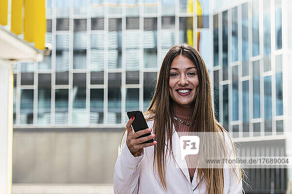 Happy woman with smart phone standing in front of building