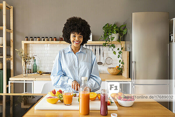 Happy beautiful woman with fruits standing in kitchen at home