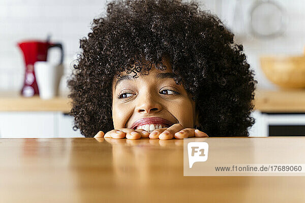 Glückliche Frau mit Afro-Frisur versteckt sich zu Hause hinter der Kücheninsel