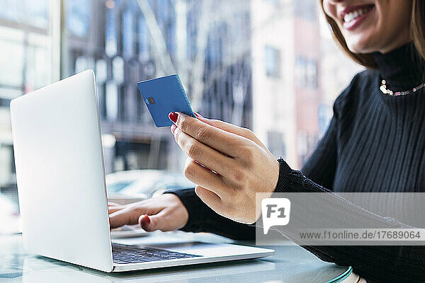 Lächelnde Geschäftsfrau sitzt mit Laptop und hält Kreditkarte in der Hand