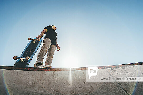 Mann mit Skateboard steht an sonnigem Tag im Skateboardpark