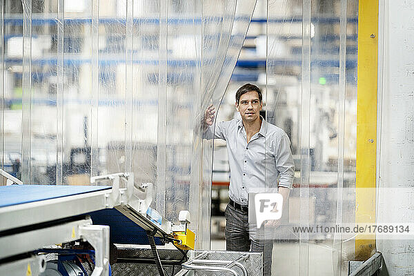 Businessman with laptop opening plastic curtain in factory