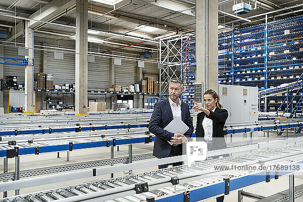 Young businesswoman discussing with colleague by conveyor belt in factory