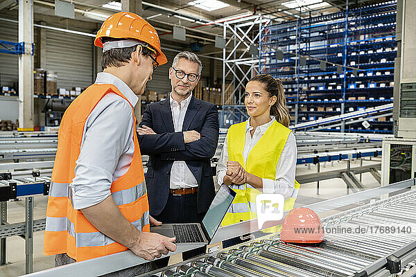 Blue-collar worker discussing with colleague by manager in factory