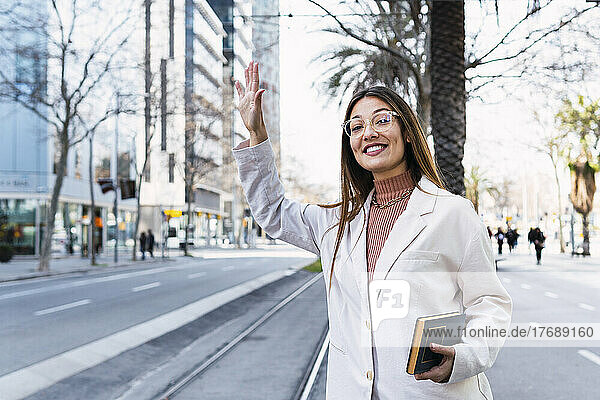 Happy woman hailing ride standing on city street