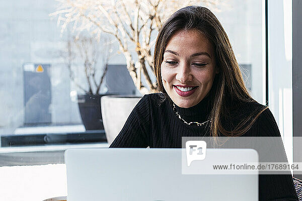 Smiling young businesswoman with brown hair using laptop in cafe
