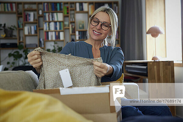 Smiling mature woman checking clothes in package on sofa at home