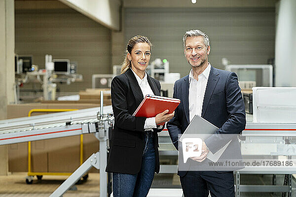 Smiling young businesswoman with businessman in factory