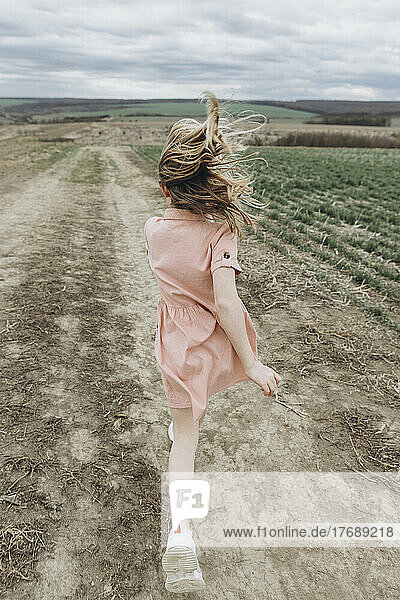 Girl running on dirt road in agricultural field