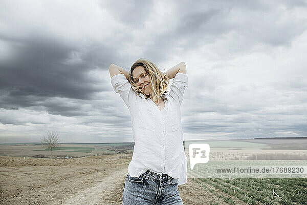 Smiling woman with arms raised standing in agricultural field