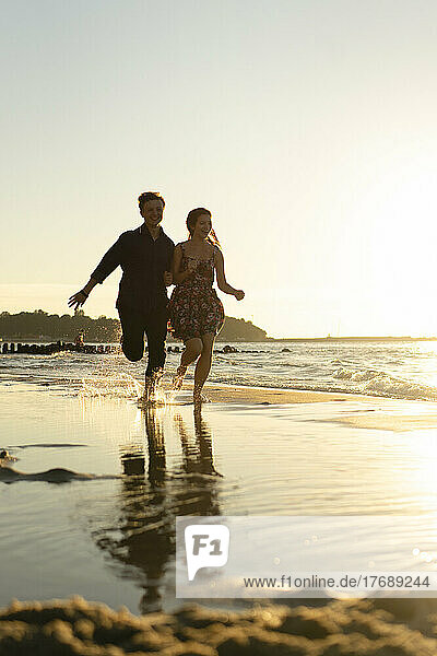 Glückliches junges Paar läuft an einem sonnigen Tag am Strand