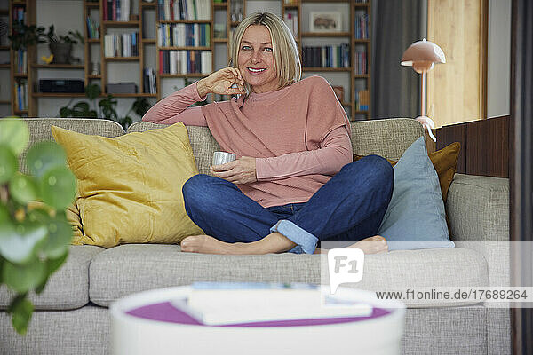Happy woman with coffee cup sitting on sofa at home