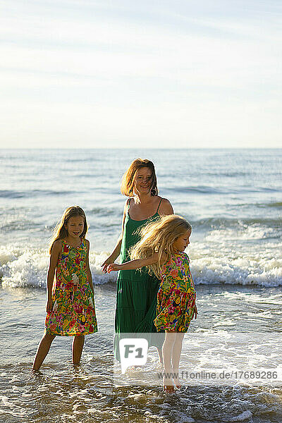 Lächelnde Mutter mit Töchtern  die sich am Strand im Wasser vergnügen