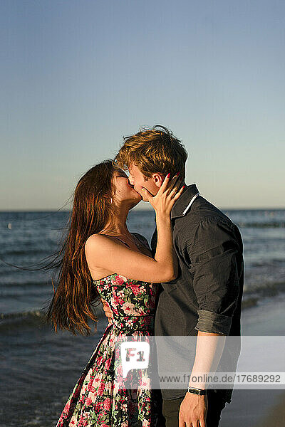 Liebevolles Paar küsst sich am Strand bei Sonnenuntergang