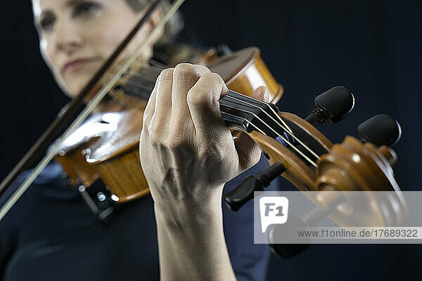 Mature woman playing violin against black background