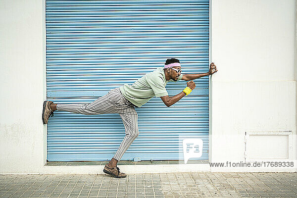 Playful young man standing on one leg in front of blue shutter