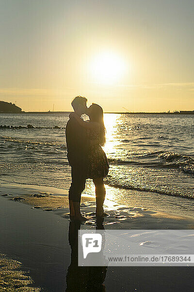 Young couple kissing each other in front of sea on beach at sunset