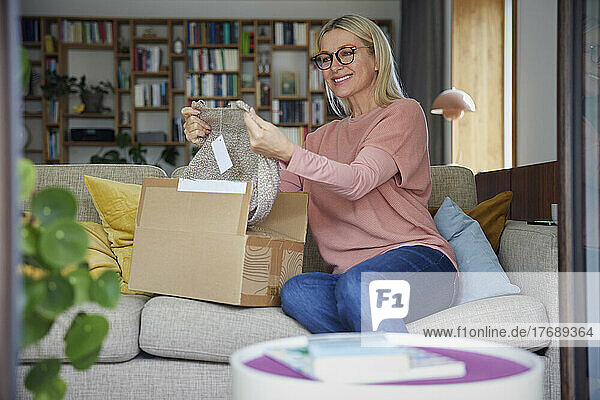 Smiling woman checking clothes in package on sofa at home
