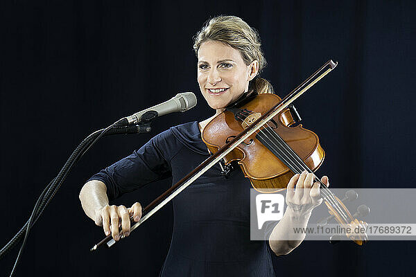 Smiling mature woman playing violin in front of black background