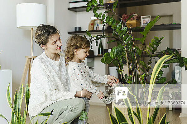 Mädchen gießt Topfpflanze mit Mutter im Wohnzimmer