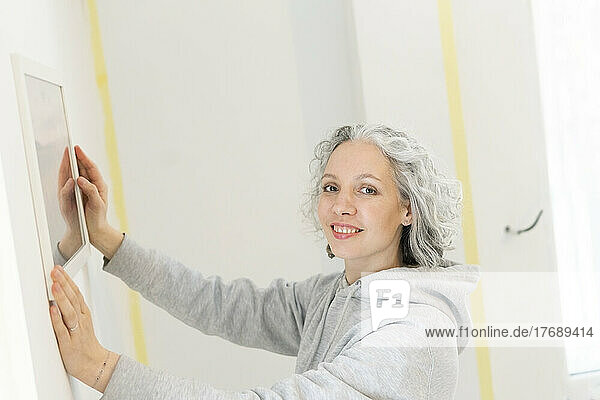 Smiling woman arranging mirror on wall