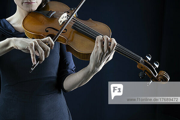 Mature woman playing violin in front of black background