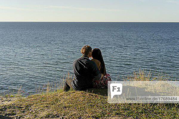 Couple sitting in front of sea on sunny day