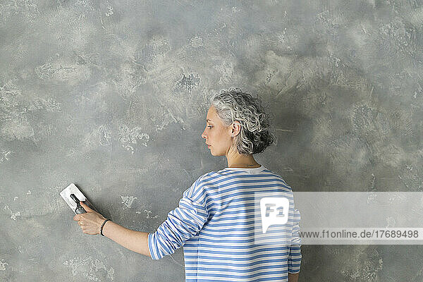 Frau mit Arbeitsgerät arbeitet an grauer Wand
