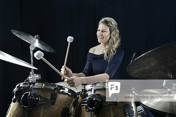 Smiling mature woman playing drums against black background