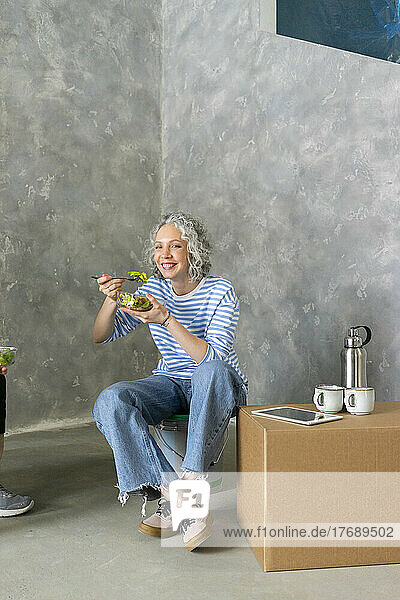 Smiling woman eating lunch in front of gray wall