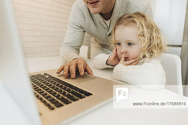 Cute daughter with father using laptop at home