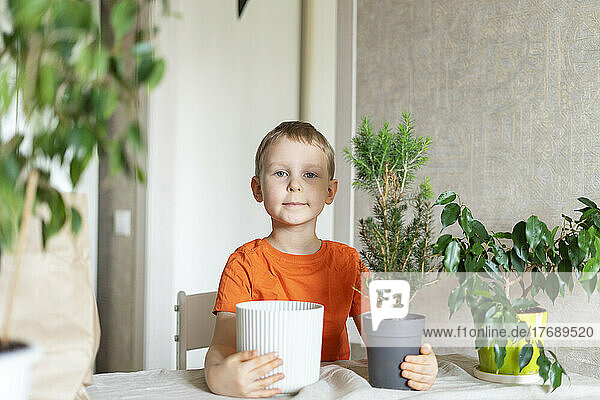Boy with pot and houseplant on table at home