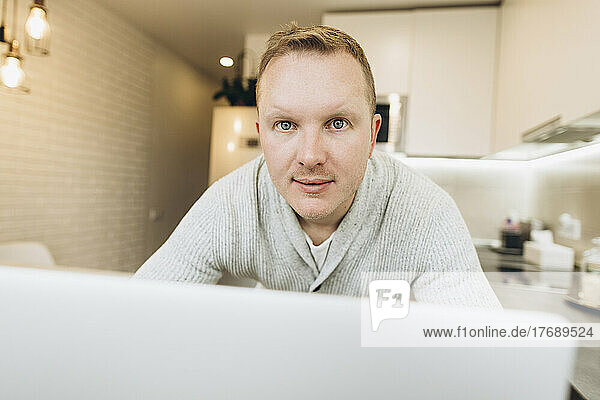 Smiling businessman with laptop in kitchen at home
