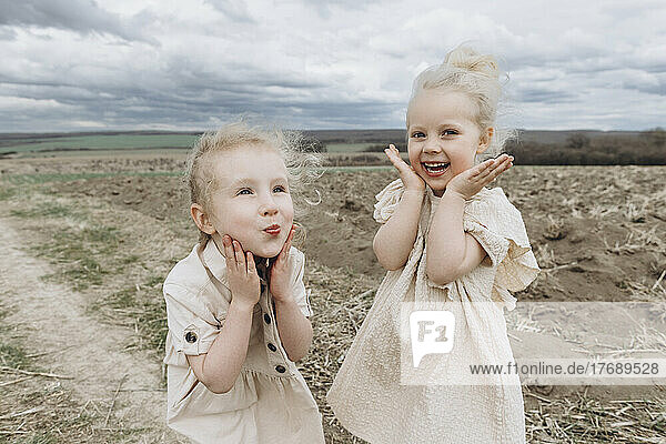 Cute happy sisters gesturing together at agricultural field