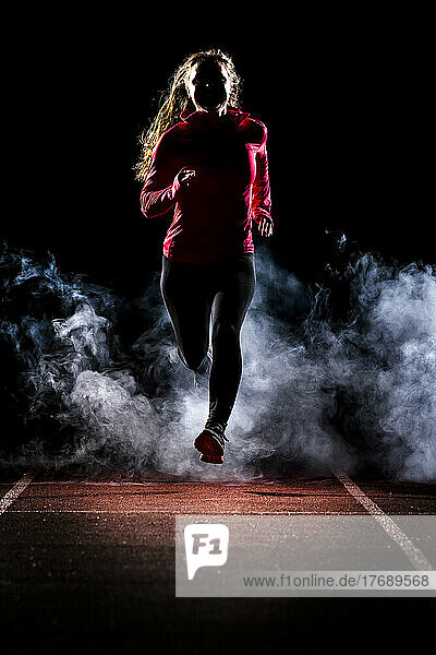 Young woman jogging on running track amidst fog in dark at night