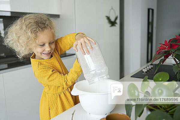 Smiling blond girl baking in kitchen at home