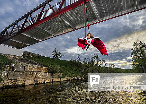 Athlete practicing aerial acrobatic hanging from bridge over Rems river