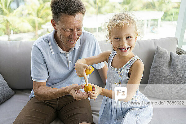 Happy daughter showing Easter eggs to father sitting on sofa at home