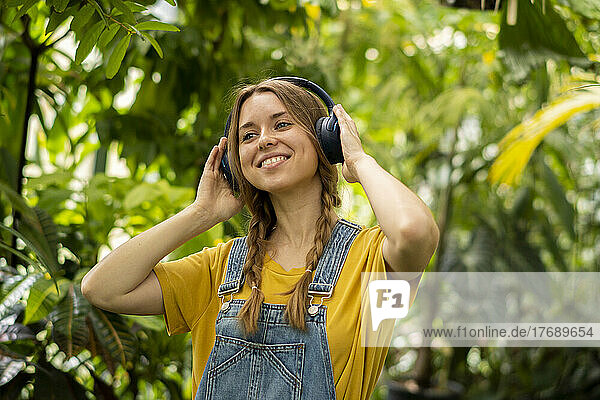 Smiling woman listening music through wireless headphones in garden