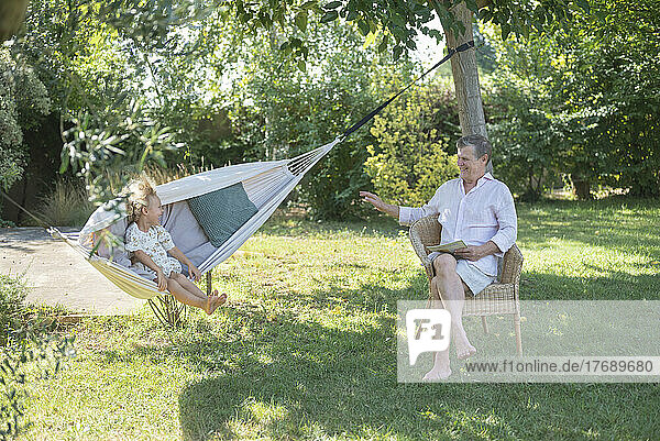 Großvater sitzt neben Enkelin und genießt Hängemattenschaukel im Garten