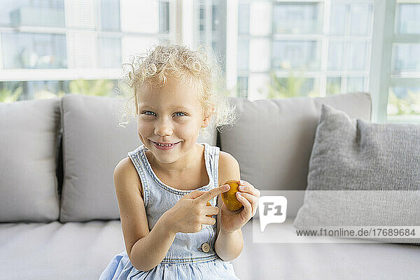 Happy cute girl pointing at Easter eggs sitting on sofa