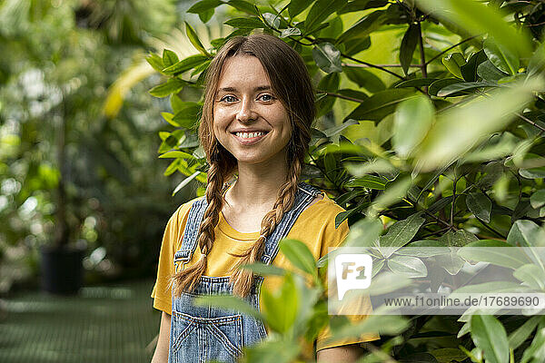 Happy young woman standing by plant in garden