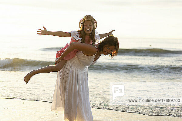 Mother giving piggyback ride to daughter enjoying at beach