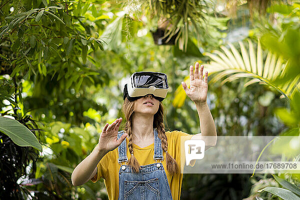 Young woman wearing virtual reality simulator gesturing in garden