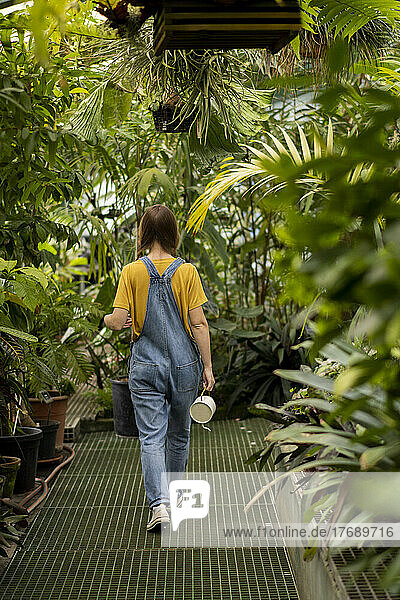 Young woman holding watering can walking amidst plant in garden