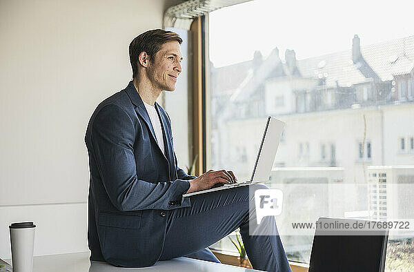Businessman using laptop at the window in office