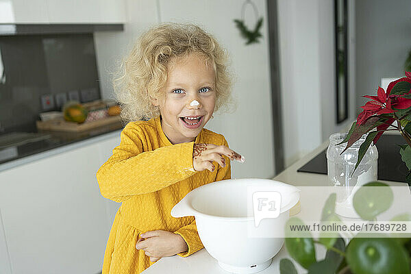 Happy blond girl with bowl standing at kitchen island