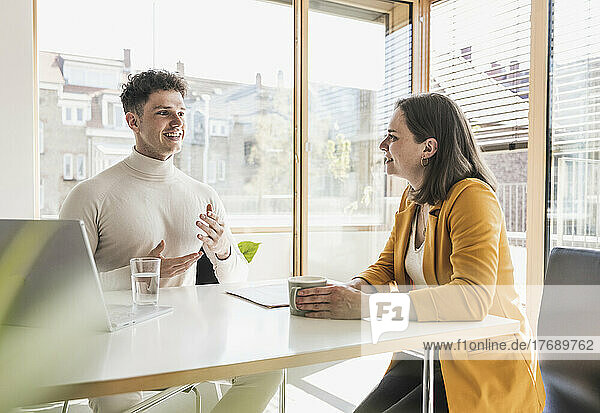 Young businessman and businesswoman talking at desk in office