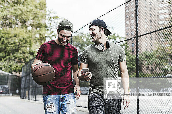 Two smiling friends with basketball outdoors